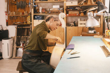 Geigenbauer beim Schnitzen eines Kontrabasses mit Handwerkzeugen in der Werkstatt - MMPF00299
