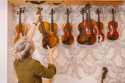 Geigenbauer beim Aufhängen von Geigen vor einer Wand im Geschäft - MMPF00306