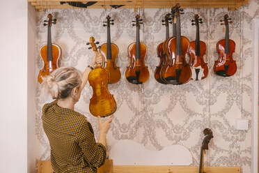 Geigenbauer begutachtet Geigen, die im Laden hängen - MMPF00307