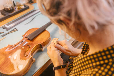 Luthier with hand tool carving wood at desk in workshop - MMPF00308