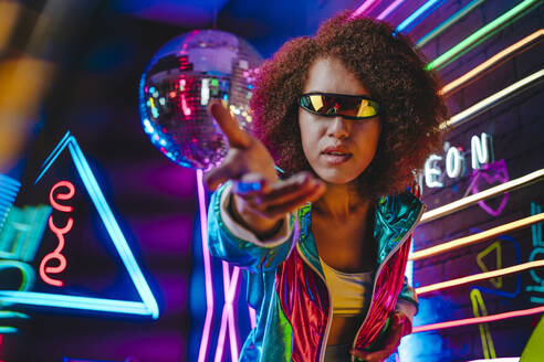 Junge Frau mit VR-Brille gestikuliert vor einem Neonlicht - YTF00105