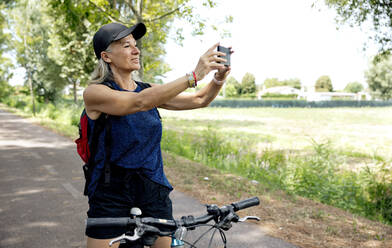 Smiling senior woman photographing through smart phone on bicycle - FLLF00708