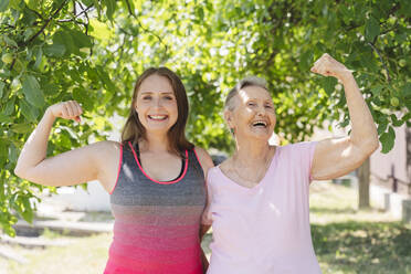 Aktive ältere Frau, die ihre Muskeln mit einem im Park stehenden Fitness-Instruktor trainiert - OSF01013