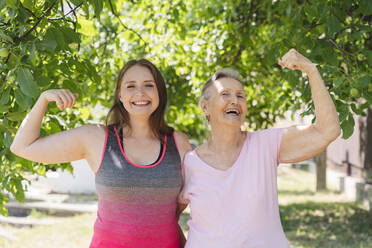 Fröhlicher Fitnesstrainer, der mit einer älteren Frau, die vor einem Baum steht, Muskeln trainiert - OSF01014