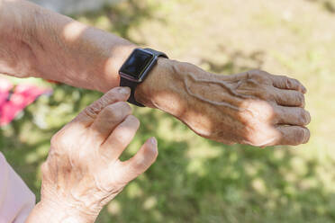 Hands of senior woman wearing smart watch on sunny day - OSF01016