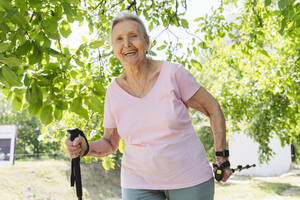 Glückliche ältere Frau, die mit einem Gehstock im Park trainiert - OSF01018