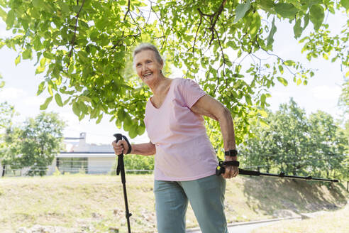 Lächelnde ältere Frau mit Wanderstock an einem Baum - OSF01020
