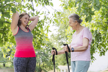 Happy fitness instructor with senior woman standing by tree - OSF01021