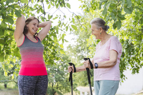 Glückliche Fitness-Trainerin mit älterer Frau, die an einem Baum steht - OSF01021