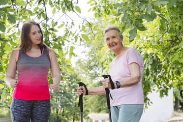 Fitness instructor teaching exercise to senior woman with walking pole in park - OSF01022