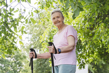 Lächelnde ältere Frau mit Wanderstock vor einem Baum stehend - OSF01023