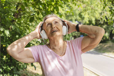 Happy senior woman listening to music and exercising in park - OSF01032