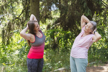 Fröhliche Fitnesstrainerin, die einer älteren Frau im Park Übungen beibringt - OSF01041