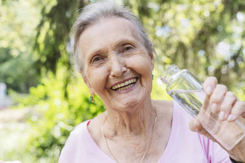 Cheerful senior woman holding water bottle at park - OSF01048