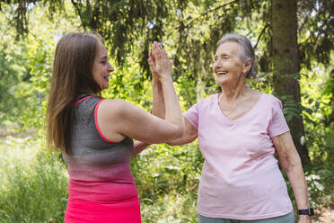 Lächelnder Fitnesstrainer berührt die Hand einer älteren Frau, die im Park trainiert - OSF01052