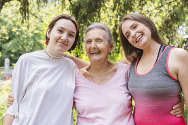 Cheerful senior woman with daughter and granddaughter standing at park - OSF01056