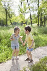 Cheerful cute girl holding hand of brother at park - ONAF00117