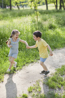 Fröhliches süßes Mädchen spielt mit Bruder im Park - ONAF00118