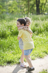 Happy girl hugging brother in park on sunny day - ONAF00120