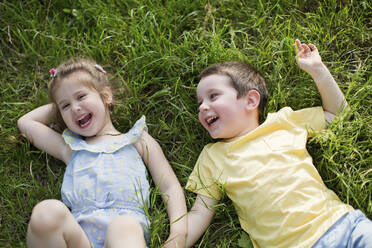 Fröhliche niedliche Geschwister entspannen sich auf dem Rasen im Park - ONAF00122