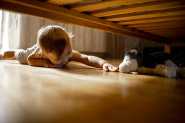 Lächelnder Junge greift nach Stofftier unter dem Bett zu Hause - ANAF00016