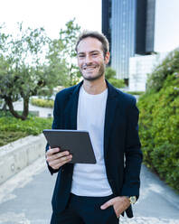 Glücklicher Geschäftsmann mit Tablet-PC im Büropark - AMRF00057