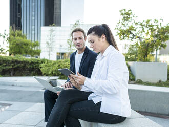 Geschäftsfrau teilt sich einen Tablet-PC mit einem Geschäftsmann, der im Büropark sitzt - AMRF00061