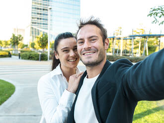 Happy businesswoman with colleague taking selfie at office park - AMRF00068