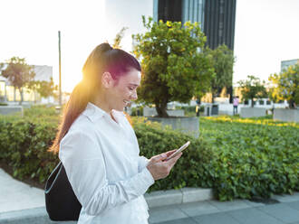 Glückliche Geschäftsfrau mit Smartphone im Büropark bei Sonnenuntergang - AMRF00069