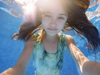 Mädchen mit langen Haaren schwimmt unter Wasser im Pool - MEGF00125