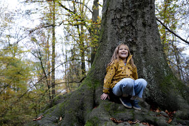 Glückliches Mädchen auf einem Baumstamm im Wald liegend - FLLF00723