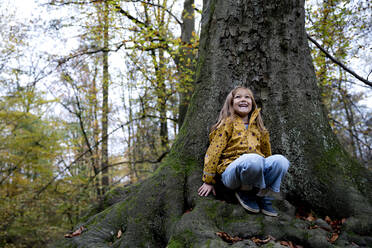 Happy girl couching on tree trunk in forest - FLLF00723