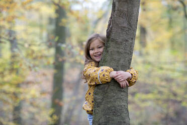 Glückliches süßes Mädchen umarmt Baum im Wald - FLLF00728