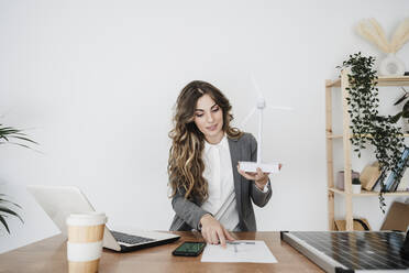 Junge Ingenieurin arbeitet in einem modernen Büro und hält ein Windturbinenmodell - EBBF06504