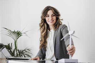 Junge Geschäftsfrau mit einem Modell einer Windturbine in einem modernen Büro - EBBF06507