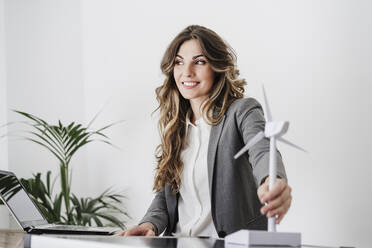 Young businesswoman holding windturbine model in modern office - EBBF06508