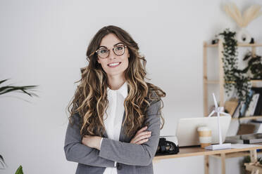 Confident businesswoman standing in office with arms crossed - EBBF06527