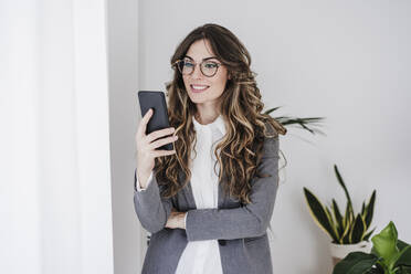 Lächelnde Geschäftsfrau, die im Büro ein Mobiltelefon benutzt - EBBF06528