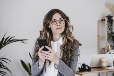 Nachdenkliche Geschäftsfrau, die im Büro ein Mobiltelefon benutzt - EBBF06532