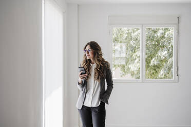 Young businesswoman standing in office using smartphone - EBBF06534