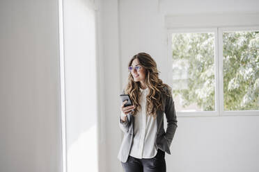 Junge Geschäftsfrau steht im Büro und benutzt ein Smartphone - EBBF06535