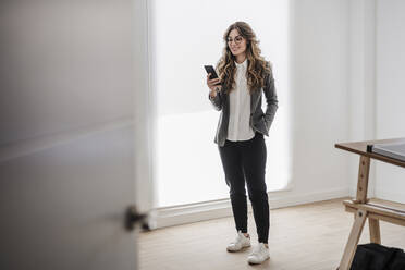 Young businesswoman standing in office using smartphone - EBBF06536
