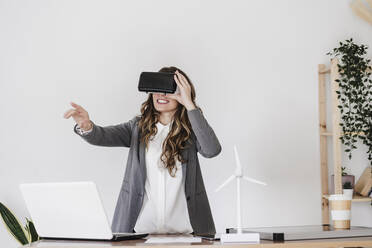 Gestikulierende junge Geschäftsfrau, die einen Simulator für virtuelle Realität im Büro benutzt - EBBF06552