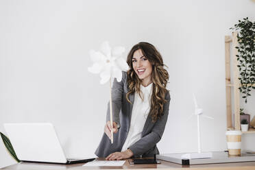 Young businesswoman holding white pinwheel toy in office - EBBF06556