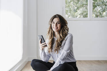 Smiling businesswoman in office using mobile phone by window - EBBF06569