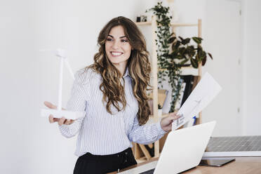 Young entrepreneur holding windturbine model in sustainable office - EBBF06578