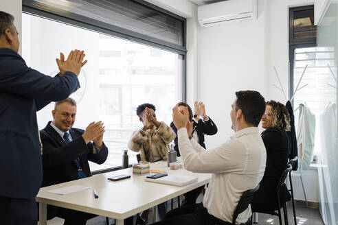 Glückliche Geschäftskollegen, die bei einem Treffen im Büro gemeinsam applaudieren - DCRF01472