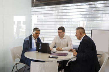 Businessman discussing over laptop with colleagues sitting at desk in office - DCRF01479