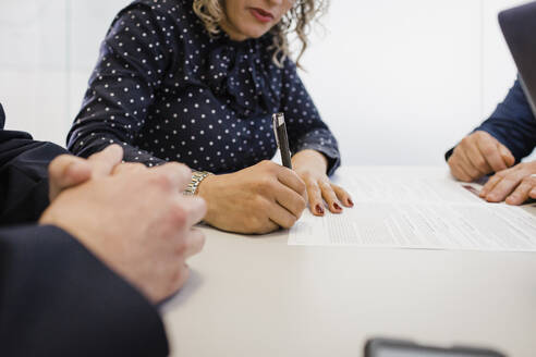 Reife Geschäftsfrau bei der Unterschrift auf einem Dokument am Schreibtisch - DCRF01483