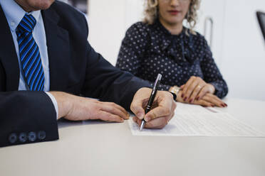 Reifer Geschäftsmann bei der Unterschrift auf einem Dokument am Schreibtisch - DCRF01488